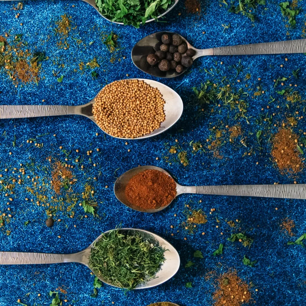 Colorful spices in spoons on a vibrant blue background, showcasing culinary variety.